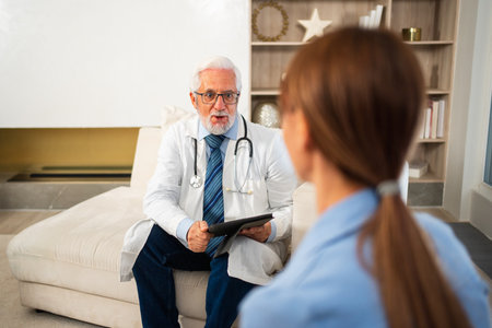 Senior man doctor examining young woman in doctor office clinic or at home. Girl patient and doctor have consultation in hospital room. Medicine healthcare medical checkup. Visit to doctorの写真素材