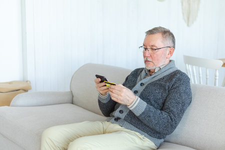 Senior man shopping online holding smartphone paying with credit card. Old grandfather buying on Internet enter credit card details. Online shopping delivery service Older generation modern tech usageの写真素材