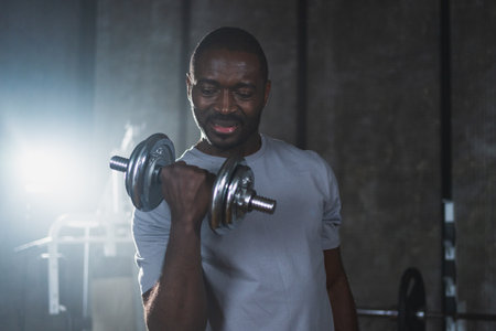 Fitness workout in gym. African American man bodybuilder picking up dumbbells in gym. Workout weight...
