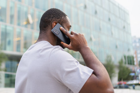 Back view African American man talking on smartphone outdoor. Unrecognizable person guy with cell...