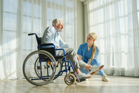 Help support retirement healthcare. Nurse helping old man in wheelchair. Patient and woman in nursing home for medical caregiver. Nurse taking care of paralyzed man in chair for people with disabilityの写真素材