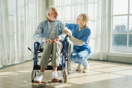 Help support retirement healthcare. Nurse helping old man in wheelchair. Patient and woman in nursing home for medical caregiver. Nurse taking care of paralyzed man in chair for people with disabilityの写真素材