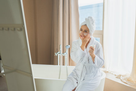 Mature adult old woman applying nourishing anti age face cream doing daily beauty routine. Senior...
