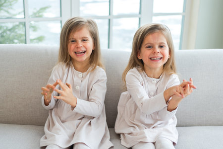 Happy family sisterly love. Two funny little twin sisters girls smiling playing together at home indoors. Happy children lifestyle. Identical twin girls. Girls friendship and youthの写真素材