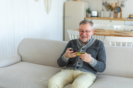 Senior man shopping online holding smartphone paying with credit card. Old grandfather buying on...