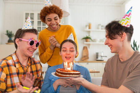 Make a wish. Woman wearing party cap blowing out burning candles on birthday cake. Happy Birthday...