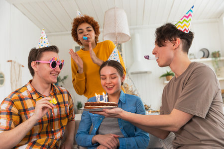 Make a wish. Woman wearing party cap blowing out burning candles on birthday cake. Happy Birthday...