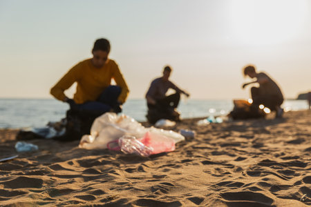 Earth day. Volunteers activists collects garbage cleaning of beach coastal zone. Woman mans with trash in garbage bag on ocean shore. Environmental conservation coastal zone cleaning. Blurred imageの写真素材