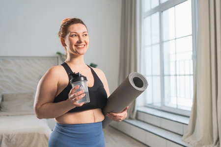 Yoga fitness sport workout training. Woman hold yoga mat bottle water ready for practicing yoga at home. Plus size female doing sports indoor. Girl in sportswear have training workout for weight lossの写真素材