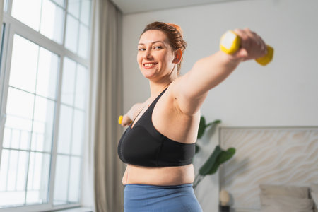 Fitness workout training. Woman picking up dumbbells. Plus size female doing sports exercise at home indoor. Girl in sportswear have workout weight training for weight loss. Sport and fitnessの写真素材