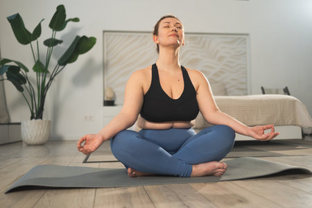 Yoga mindfulness meditation. Woman practicing yoga in living room at home. Female sitting in lotus pose meditating smiling relaxing indoor. Girl doing breathing practice. Yoga at homeの写真素材