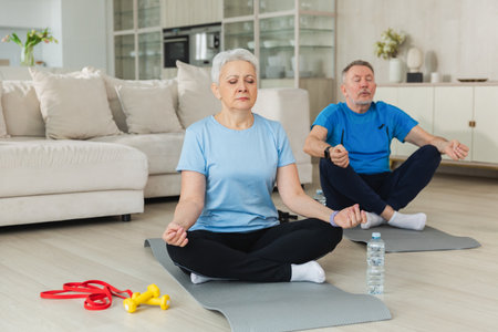 Yoga mindfulness meditation. Senior adult mature couple practicing yoga at home. Mid age old husband wife sitting in lotus pose on yoga mat meditating relaxing. Family doing breathing practiceの写真素材