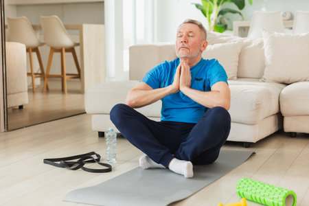 Yoga mindfulness meditation. Senior adult mature man practicing yoga at home. Mid age old grandfather sitting in lotus pose on yoga mat meditating relaxing. Older man doing breathing practiceの写真素材