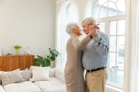 Keep moving. Romantic senior mature couple dancing to music together at home. Happy smiling family retired man woman husband wife having fun enjoying time together. Family moment love careの写真素材