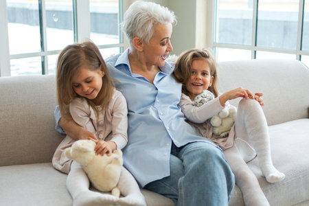 Happy family at home. Two little girls sisters twins grandmother enjoying time together. Good time at home. Grandma granddaughters child kids emotional bonding hugging together. Family generationsの写真素材