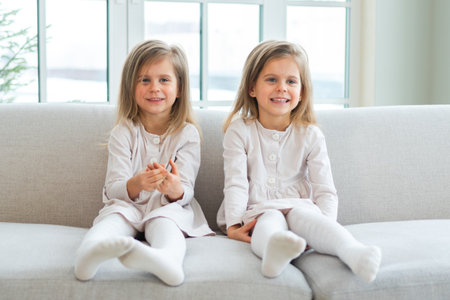Happy family sisterly love. Two funny little twin sisters girls smiling playing together at home indoors. Happy children lifestyle. Identical twin girls. Girls friendship and youthの写真素材