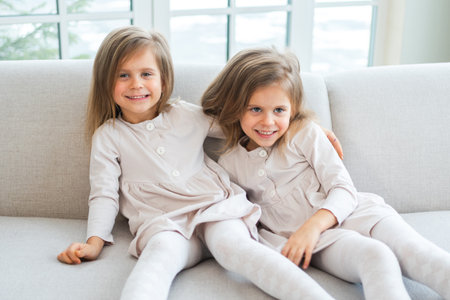 Happy family sisterly love. Two funny little twin sisters girls smiling playing together at home indoors. Happy children lifestyle. Identical twin girls. Girls friendship and youthの写真素材