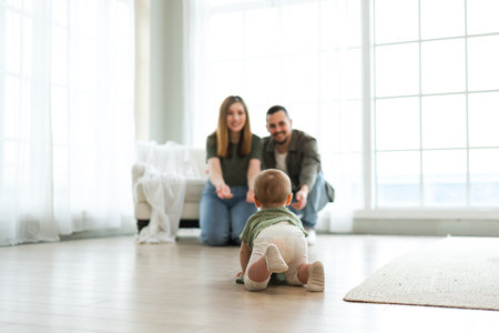 Happy family. Mother father looking at cute little toddler girl crawling on floor in bedroom. Infant...