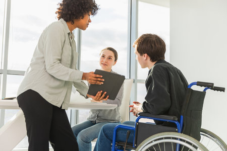 Teamwork brainstorm. Diverse multiracial colleagues man in chair for people with disability working together. Group of people sitting in creative office discussing business. Young professional teamの写真素材