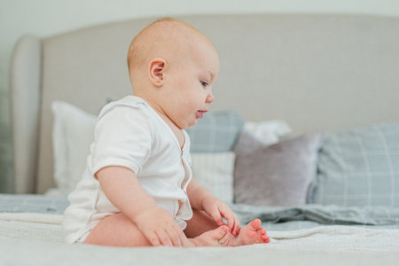 Happy baby. Cute little newborn girl with smiling face sitting on bed in bedroom. Infant baby...