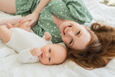 Happy family at home. Mother playing with little toddler child on bed. Mom baby relax playing having fun together. Mother looks at camera with love care. Mom of baby rest in living roomの写真素材