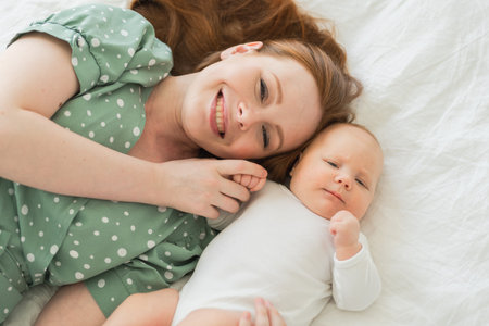 Happy family at home. Mother playing with little toddler child on bed. Mom baby relax playing having...