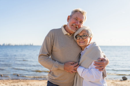 Senior mature couple hugging enjoying outdoor recreation walking on beach. Old husband wife...