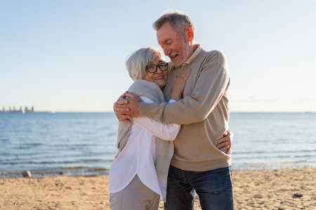 Senior mature couple hugging enjoying outdoor recreation walking on beach. Old husband wife embracing with tenderness love enjoying sweet bonding. Grandmother grandfather together. Family moment loveの写真素材