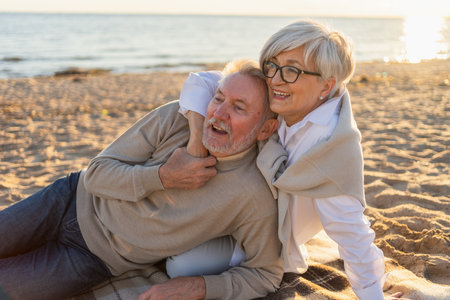 Senior mature couple sitting on beach hugging enjoying outdoor recreation. Old husband wife embracing with tenderness love enjoying sweet bonding. Grandmother grandfather together. Family moment loveの写真素材