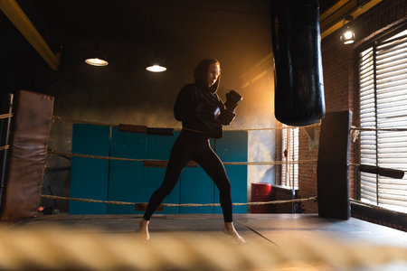 Women self defense girl power. Strong woman fighter training punches on boxing ring. Healthy strong girl punching boxing bag. Training day in boxing gym. Strength fit body workout trainingの写真素材