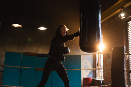 Women self defense girl power. Strong woman fighter training punches on boxing ring. Healthy strong girl punching boxing bag. Training day in boxing gym. Strength fit body workout trainingの写真素材