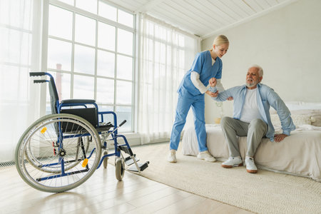 Rehabilitation healthcare. Physiotherapist nurse helps old man patient in wheelchair stand up walking. Man in chair for people with disability doing few steps with nurse helping. Medical caregiverの写真素材