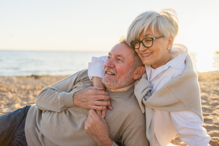 Senior mature couple sitting on beach hugging enjoying outdoor recreation. Old husband wife embracing with tenderness love enjoying sweet bonding. Grandmother grandfather together. Family moment loveの写真素材