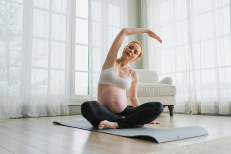 Pregnancy yoga fitness workout training. Pregnant woman practicing yoga at home. Pregnant girl doing sports exercise on yoga mat indoor. Woman with big belly have fitness training practicing asanaの写真素材