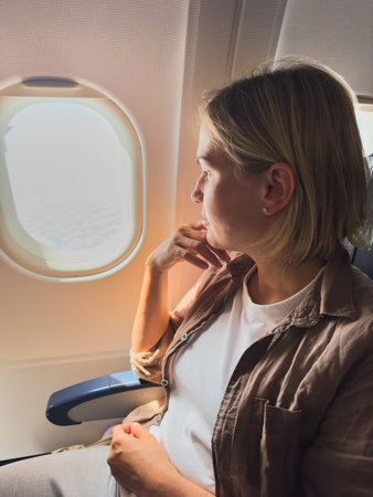 Passenger woman is flying in plane. Girl sitting in airplane looking out window going on trip vacation travel. Traveling female inside plane enjoying flight. Traveling girlの写真素材