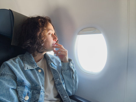 Happy passenger woman is flying in plane. Girl sitting in airplane looking out window going on trip vacation travel. Traveling female inside plane enjoying flight. Traveling girlの写真素材