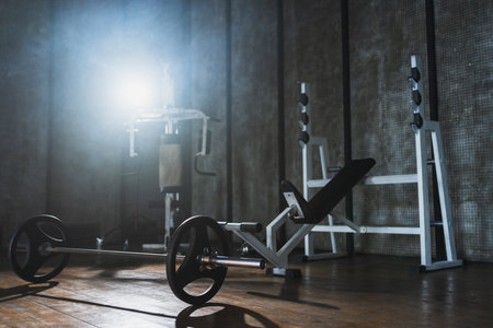 Empty gym workout area health club. Dark interior of gym with fitness equipment barbell. Weights of fitness sports for exercise. Machines tools for exercising. Training for strength building wellnessの写真素材