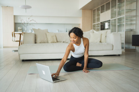 Yoga fitness workout training online. African woman practicing yoga with online lessons in laptop at home. Girl doing sports exercise on yoga mat. Woman have workout for weight loss. Sport fitnessの写真素材