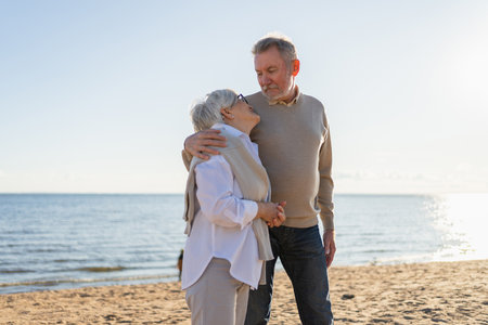 Senior mature couple hugging enjoying outdoor recreation walking on beach. Old husband wife embracing with tenderness love enjoying sweet bonding. Grandmother grandfather together. Family moment loveの写真素材