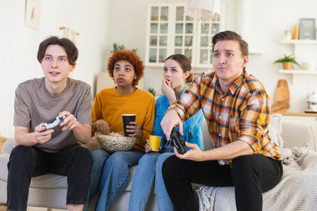 Home party. Cheerful group of friends playing video games at home. Happy diverse group buddies having fun together indoor. Friendship leisure entertainment concept. Young best friends enjoying weekendの写真素材