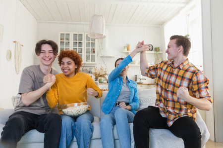 Group of friends watching sport match soccer football game on tv. Happy football fans celebrating victory at home. Friendship sports entertainment concept. Diverse buddies having fun together at homeの写真素材