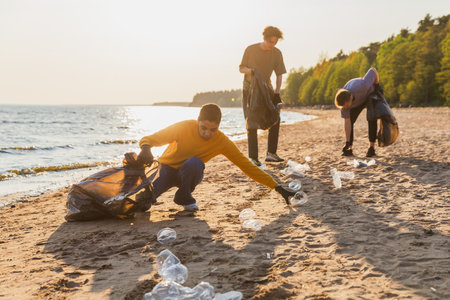 Earth day. Volunteers activists team collects garbage cleaning of beach coastal zone. Woman mans puts plastic trash in garbage bag on ocean shore. Environmental conservation coastal zone cleaningの写真素材