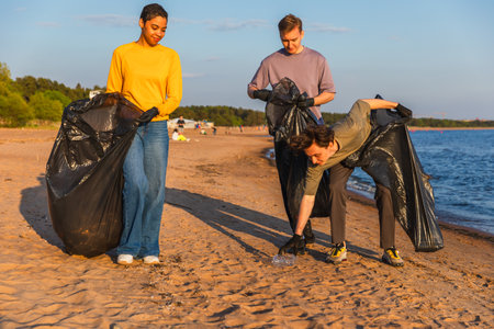 Earth day. Volunteers activists team collects garbage cleaning of beach coastal zone. Woman mans with trash in garbage bag on ocean shore. Environmental conservation coastal zone cleaningの写真素材