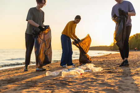 Earth day. Volunteers activists team collects garbage cleaning of beach coastal zone. Woman mans with trash in garbage bag on ocean shore. Environmental conservation coastal zone cleaningの写真素材