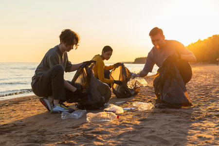 Earth day. Volunteers activists team collects garbage cleaning of beach coastal zone. Woman mans puts plastic trash in garbage bag on ocean shore. Environmental conservation coastal zone cleaningの写真素材
