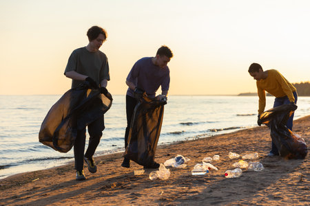 Earth day. Volunteers activists team collects garbage cleaning of beach coastal zone. Woman mans with trash in garbage bag on ocean shore. Environmental conservation coastal zone cleaningの写真素材