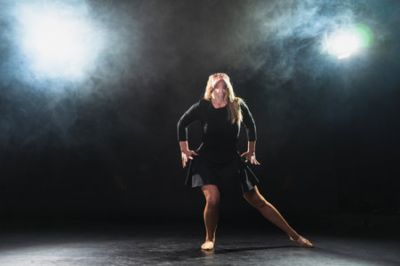 Contemporary woman dancer posing on black background with smoke. Adult female artist performer dancing with expression. Modern ballerina dancing in darkness. Passion dance in dark. Flexibility balanceの写真素材