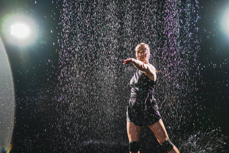 Contemporary woman dancer posing in rain water on black background. Female artist performer dancing with expression. Modern ballerina dancing in darkness. Passion dance in dark. Flexibility balanceの写真素材