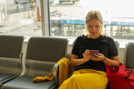 Airport terminal. Woman waiting for flight using smartphone. Girl with cell phone in airport surfing internet social media apps. Traveling female in boarding lounge of airline hub. Traveling girlの写真素材