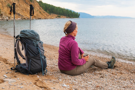 Hiking tourism adventure. Backpacker woman resting after hiking looking at beautiful view. Hiker girl lady tourist with backpack sitting near lake. Hiker woman enjoy hike tourism active vacationの写真素材